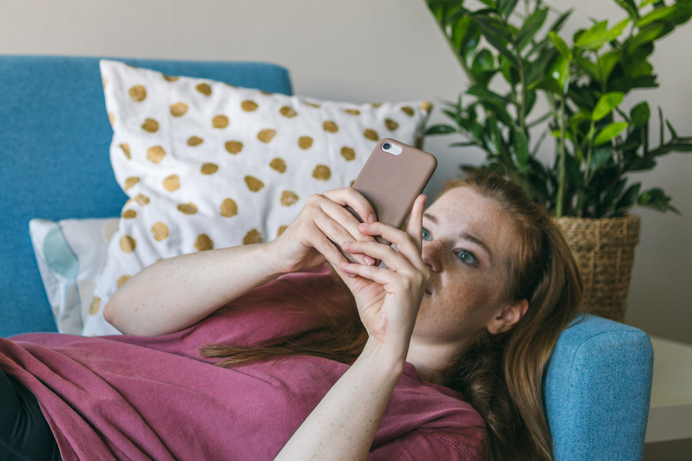 Young,Woman,Looks,Into,The,Smartphone,Screen,While,Lying,On