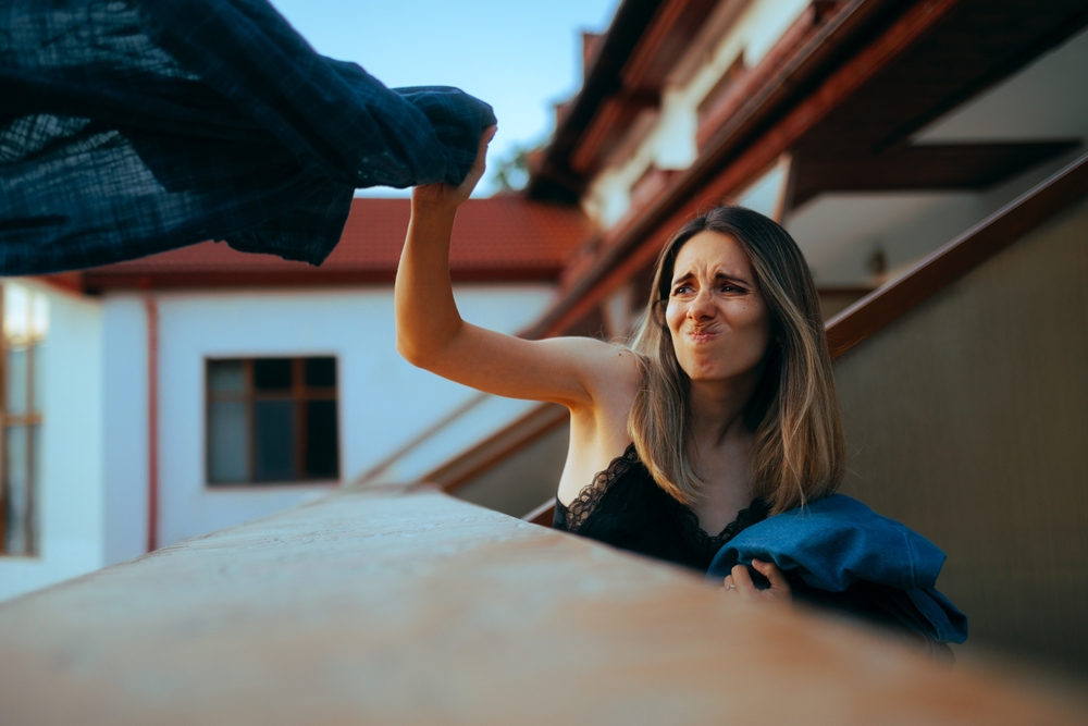 Furious,Girlfriend,Throwing,Boyfriend,Clothes,Over,The,Balcony.,Angry,Woman